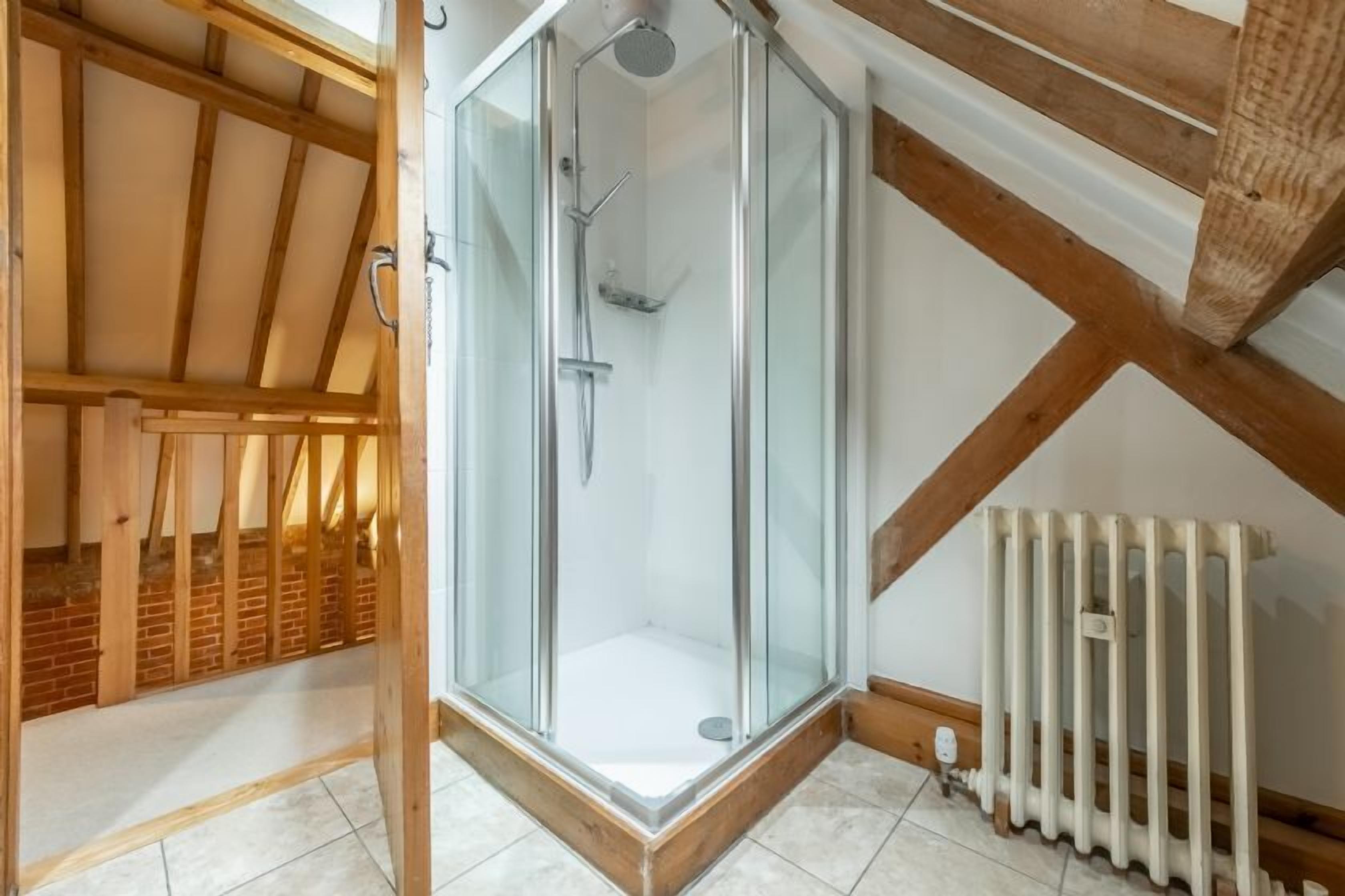 Baño con ducha envuelta en vidrio, techo de madera y radiador.