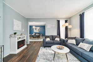 A living room with a fireplace, two sofas, a coffee table, and a dining area in the background.
