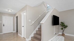 A home interior with a staircase, a flat-screen TV mounted on the wall, a potted plant, and a white furry rug on the floor. - Price Drop! Entire 4BR[10% OFF]Home| Wi-Fi & More-MD (Cypress)
