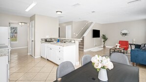 A modern kitchen with white cabinets, a granite countertop, and a dining area with a black table and grey chairs. - Price Drop! Entire 4BR[10% OFF]Home| Wi-Fi & More-MD (Cypress)