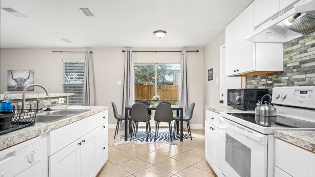 A modern kitchen with white cabinets, a granite countertop, a stainless steel kettle, and a dining table with chairs. - Price Drop! Entire 4BR[10% OFF]Home| Wi-Fi & More-MD (Cypress)