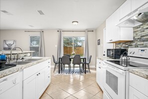 A modern kitchen with white cabinets, a granite countertop, a stainless steel kettle, and a dining table with chairs.