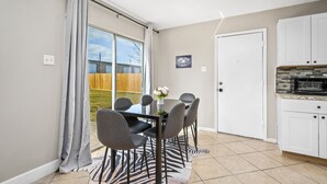 A dining area with a table and chairs, a zebra-patterned rug, a white door, and a kitchen with white cabinets and a stone backsplash. - Price Drop! Entire 4BR[10% OFF]Home| Wi-Fi & More-MD (Cypress)