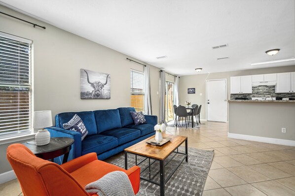 A modern living room with a blue sofa, orange armchair, and a wooden coffee table.