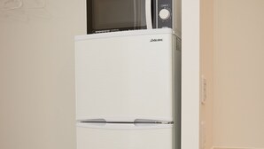 A white refrigerator with a microwave on top, a wooden shelf, and a wall-mounted light switch.