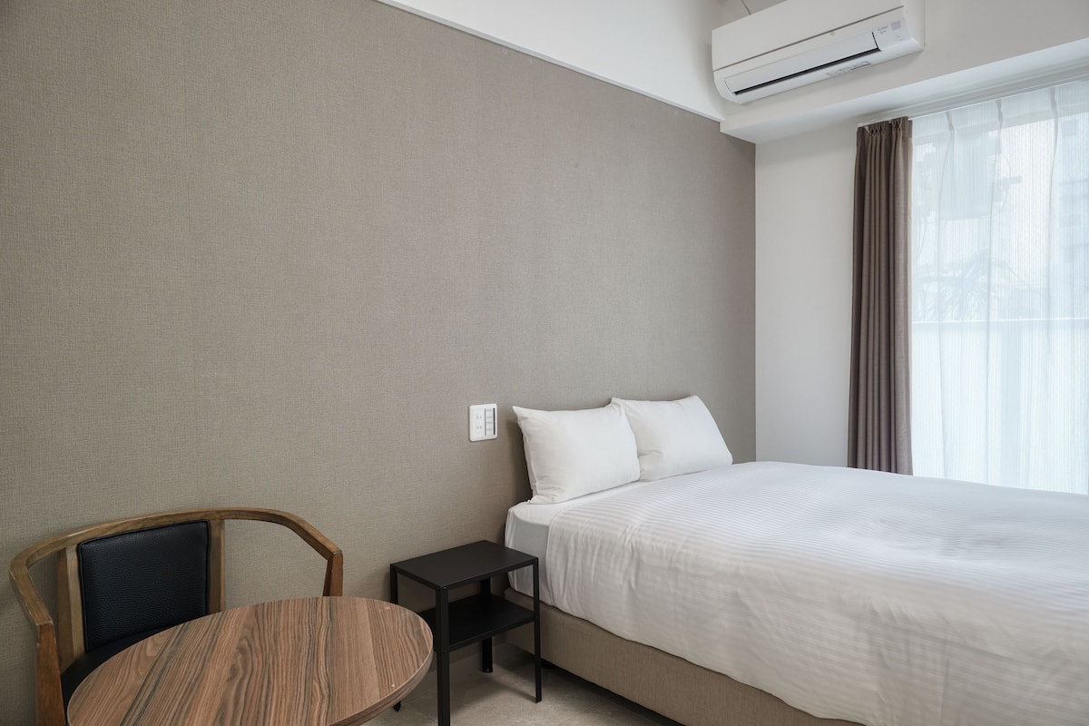 Habitación de hotel con cama, una mesita, una silla y un equipo de aire acondicionado.