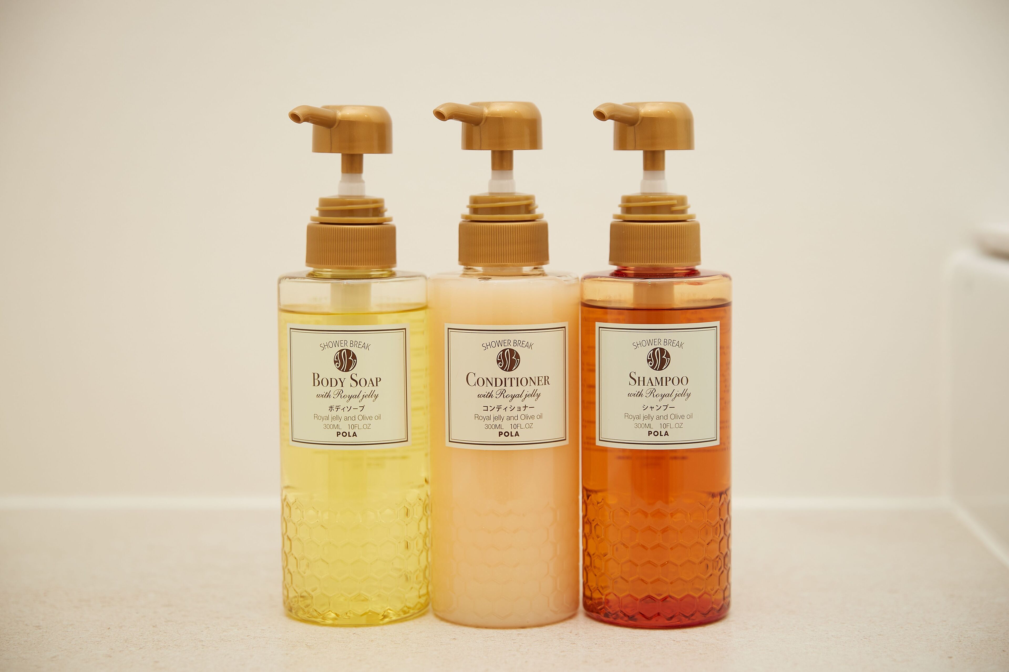 Three bottles of shower products with pumps, labeled as 'Shower Break Royal Jelly and Olive Oil', 'Conditioner with Royal Jelly', and 'Shampoo with Royal Jelly'.