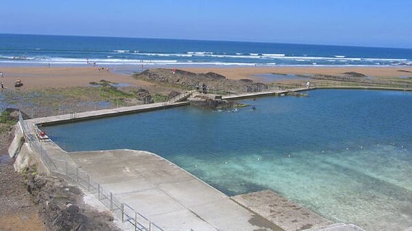 A large swimming pool with clear water, surrounded by a concrete deck and a rocky shoreline.