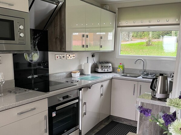 A compact kitchen with a microwave, toaster, and oven. There is a window with a view of greenery outside.