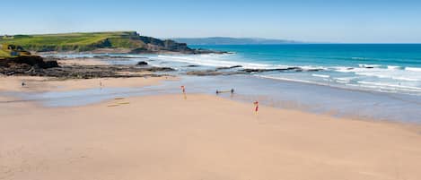 A beach with clear skies, calm waters, and rocky outcrops.
