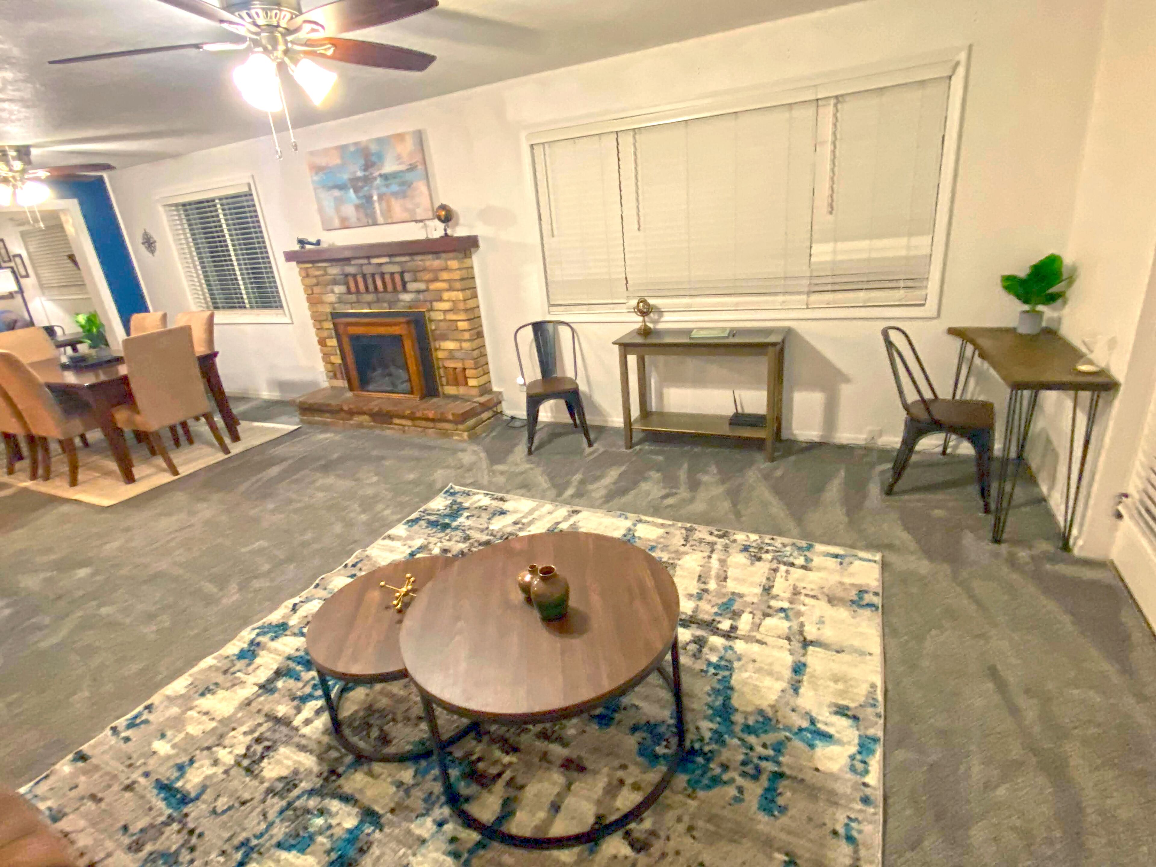 A living room with a fireplace, a dining area with chairs, a coffee table, and a ceiling fan.