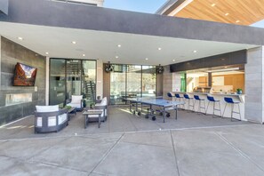 A modern outdoor dining area with a ping pong table, seating, and a kitchen area with bar stools. - Eleanor at Copper Rock Golf Course, Private Pool, 2 Hot Tubs, Basketball Court, and more (Hurricane)