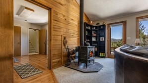 Una habitación acogedora con paredes de madera, chimenea, estantería y vistas al exterior.