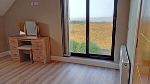 Una stanza con una scrivania in legno, uno specchio e un'ampia finestra vista su un campo.