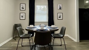 Un comedor con una mesa redonda, cuatro sillas, una araña y obras de arte enmarcadas en las paredes.