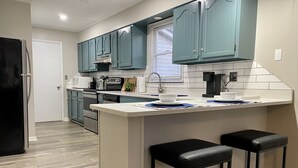 Una cocina moderna con gabinetes color turquesa, encimera blanca y dos taburetes negros.
