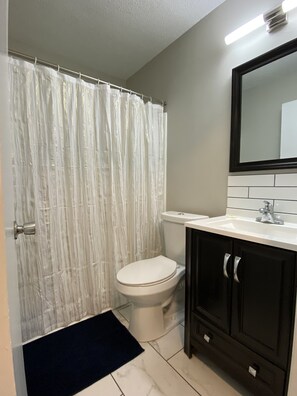 A bathroom with a white toilet, a dark wooden cabinet, a white sink, and a shower curtain. - 3 bed 2 bath single level home in Kernersville (Kernersville)
