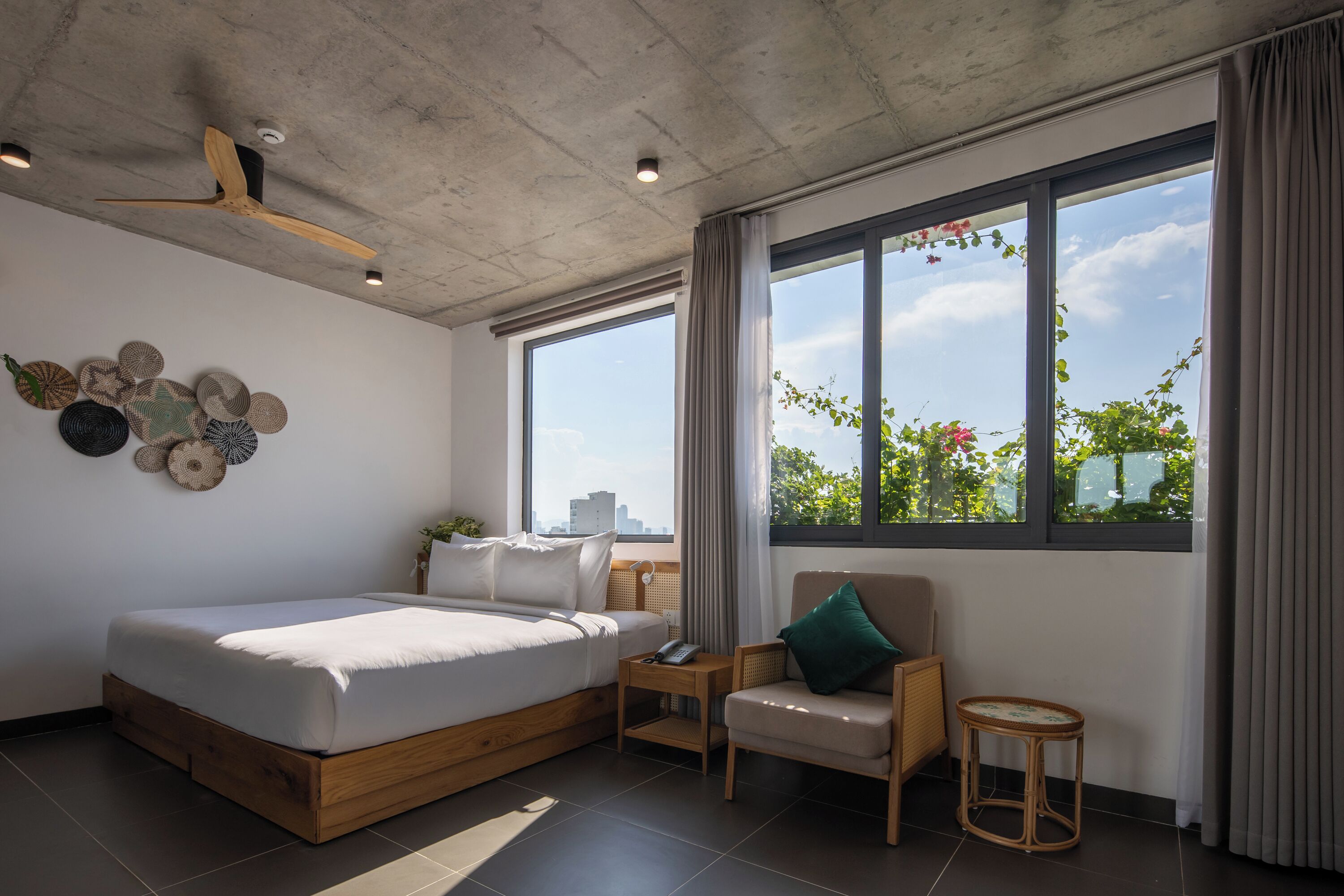 A modern bedroom with a large bed, a chair, a small table, and a window with a city view.