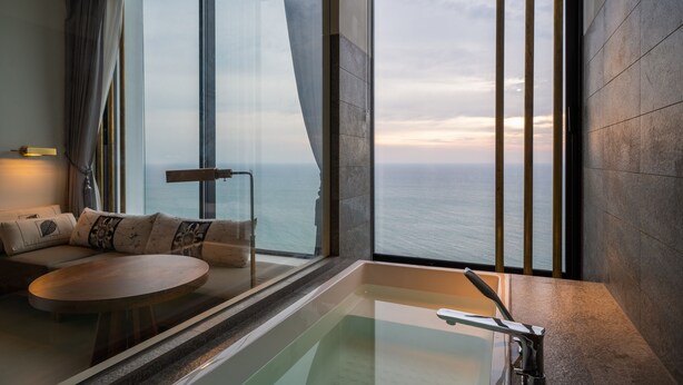 Una habitación moderna con un ventanal grande, una mesa redonda, un sofá con cojines estampados y una bañera.