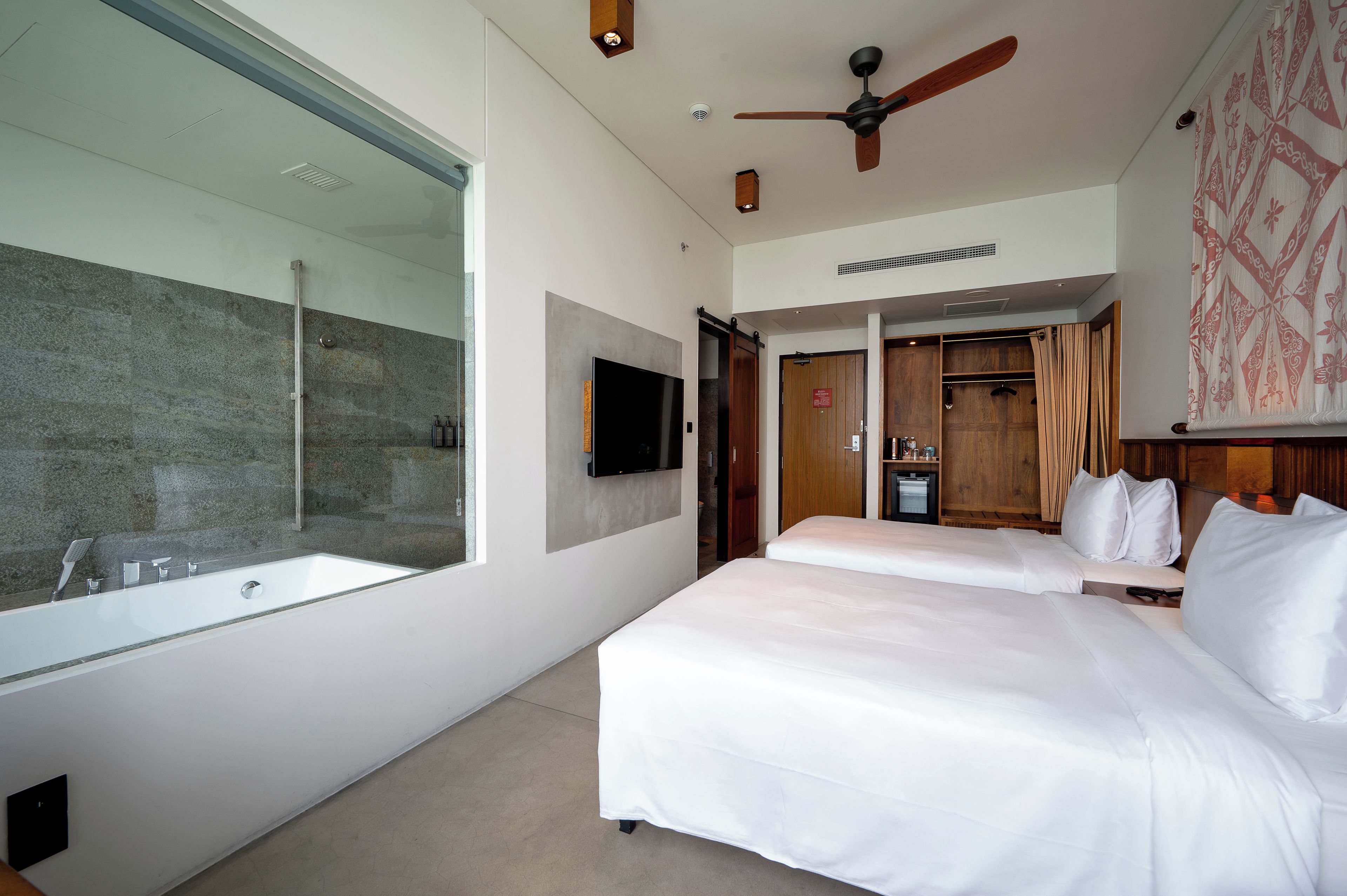 Habitación de hotel con un espejo grande, una bañera, un ventilador de techo y un armario.