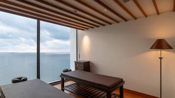 Enjoy a serene retreat with a panoramic sea view from this peaceful room, featuring a large window, a comfortable bench, and a floor lamp.