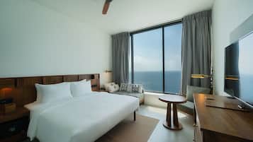 Habitación de hotel con una cama grande, un escritorio, una silla, un televisor y vistas al océano.