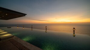 Piscina infinita con vista al atardecer, zona cubierta y tres faroles iluminados.