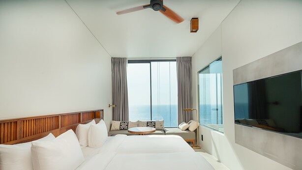 Una habitación de hotel con una cama grande, una mesa redonda, un sofá, un televisor y vistas al océano.
