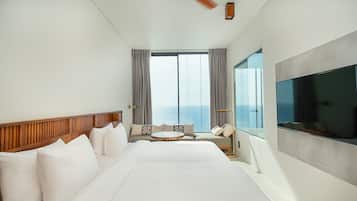 Hotelkamer met een groot bed, een ronde tafel, een bank, een televisie en uitzicht op de oceaan.