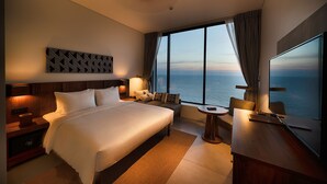 Una habitación de hotel moderna con una cama grande, un escritorio, una silla, un televisor y vistas al océano.