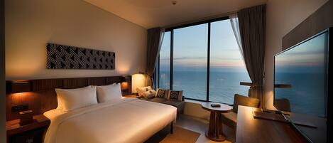 Una habitación de hotel moderna con una cama grande, un escritorio, una silla, un televisor y vistas al océano.