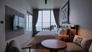 Una habitación de hotel moderna con una cama grande, un sofá, una mesa redonda, un televisor y vista al océano.