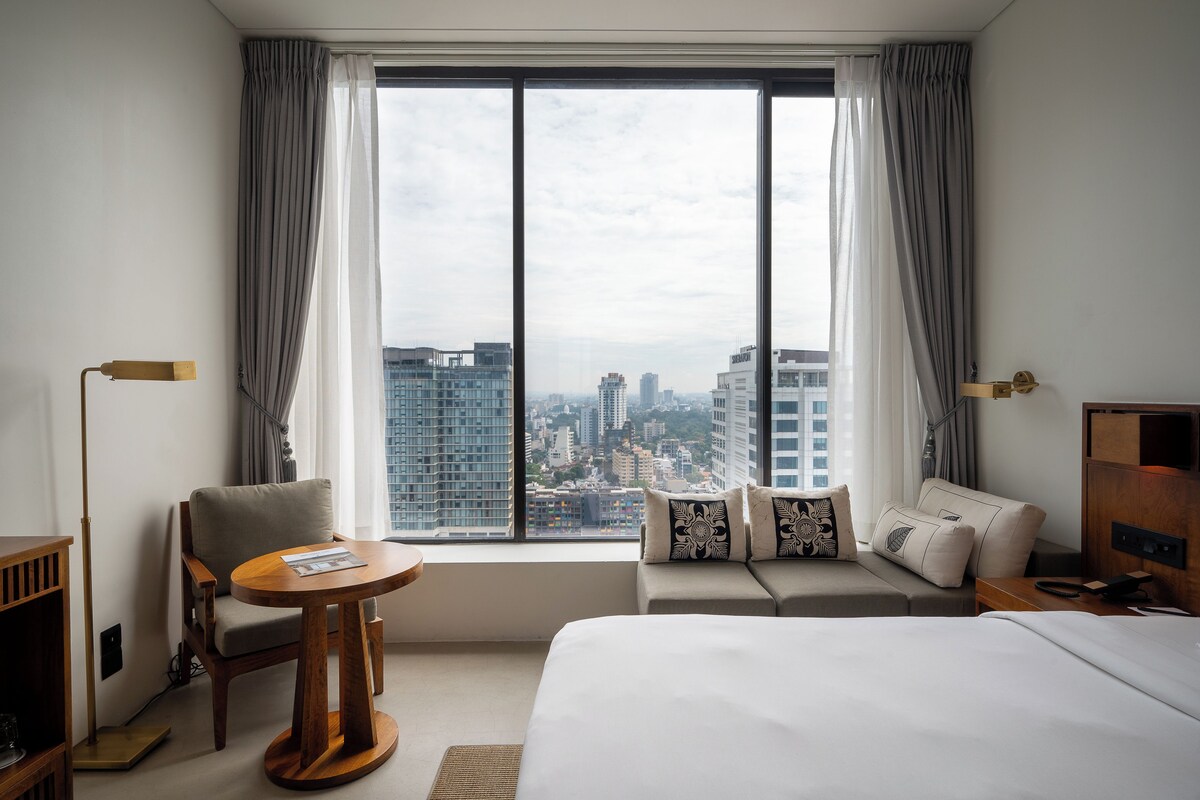 A hotel room with a bed, a sofa, a chair, a small table, and a desk with a lamp.