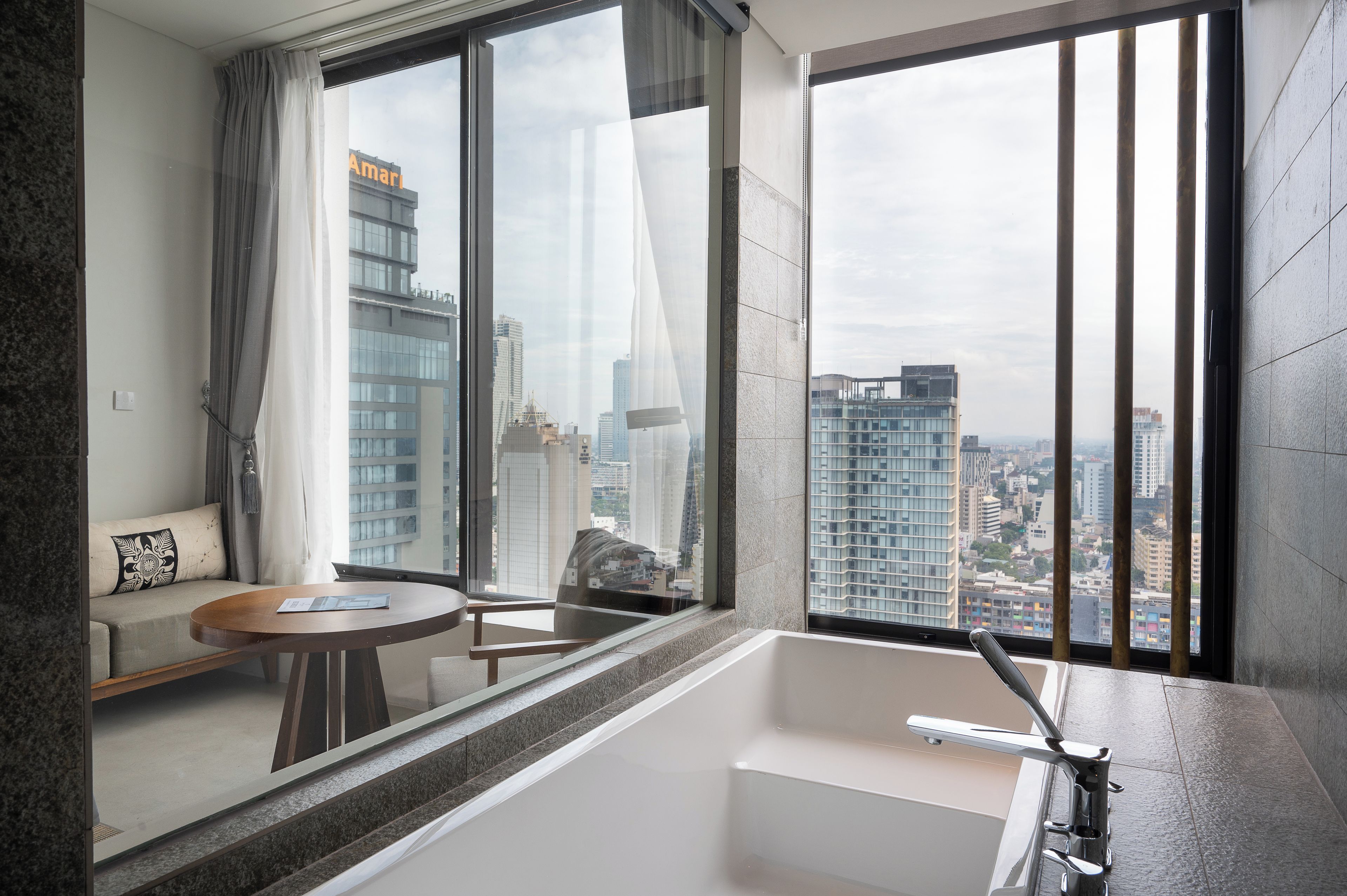 Una habitación de hotel moderna con un ventanal grande, un sofá, una mesita y una bañera.