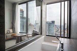 Una habitación de hotel moderna con un ventanal grande, un sofá, una mesita y una bañera.
