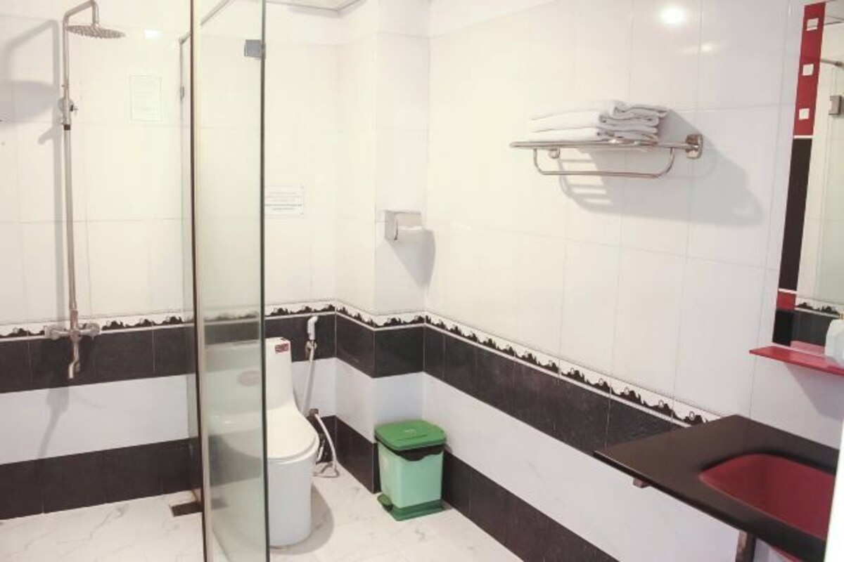 Une salle de bain avec une douche à parois de verre, des toilettes, une poubelle verte et un lavabo rouge.