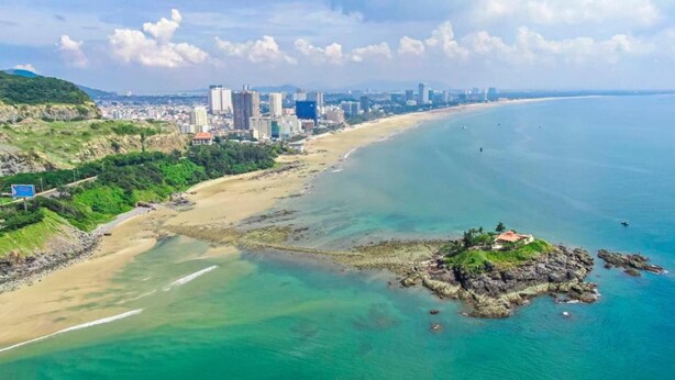 Luftaufnahme einer Küstenstadt mit Strand, Gebäuden und einer Felsformation.