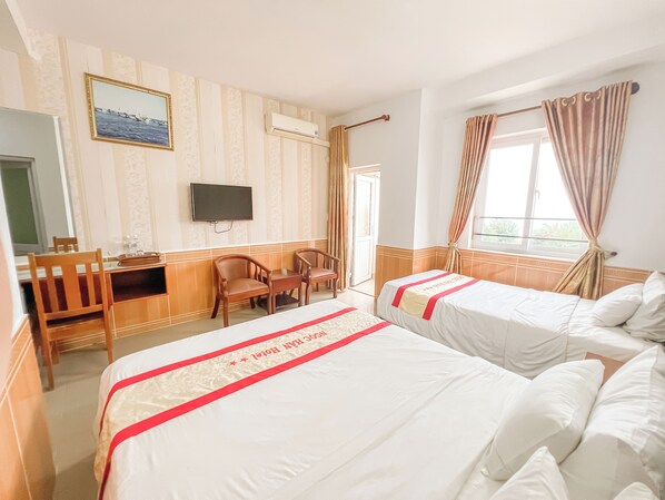 A hotel room with two beds, a desk, a chair, a television, and a window with curtains.