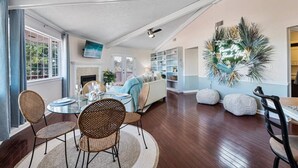 Un salon spacieux avec une cheminée, un coin repas avec des chaises en osier et une grande plante décorative.