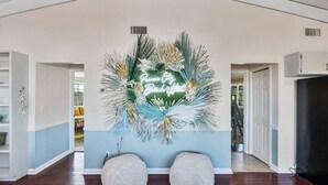 Une pièce spacieuse avec un plafond haut, une grande fresque murale représentant une végétation tropicale et deux poufs texturés adossés au mur.