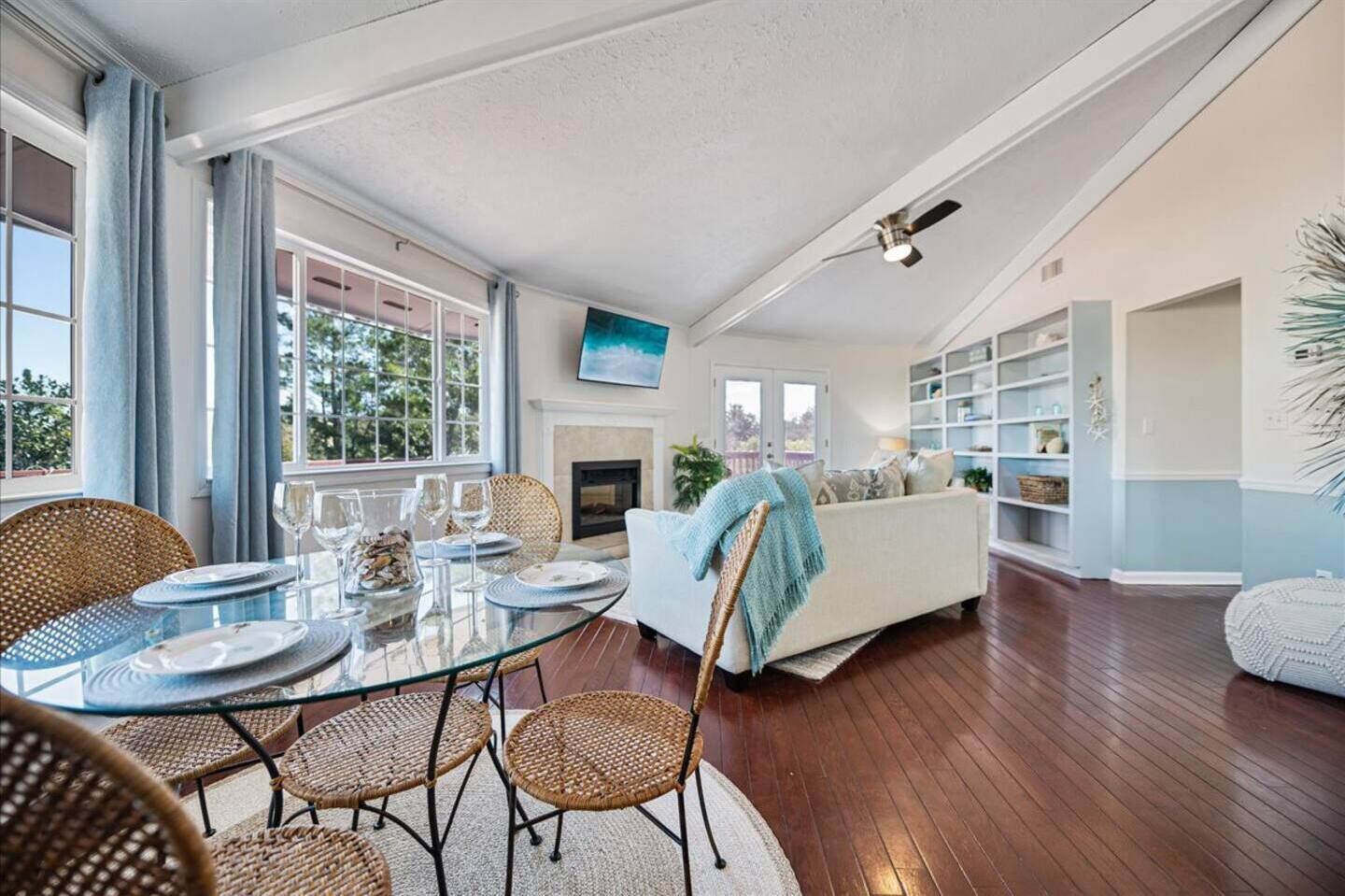 A spacious living room with a glass dining table, wicker chairs, a white sofa, and a fireplace.