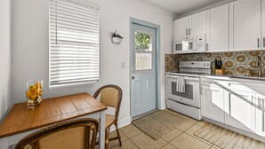 A kitchen with white cabinets, a microwave, an oven, and a dining area with a table and chairs. - "Sunflower Cottage Apt" 2/1 (West Palm Beach)