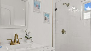 A bathroom with a white vanity, gold fixtures, a toilet, and a shower with a glass door. - "Sunflower Cottage Apt" 2/1 (West Palm Beach)