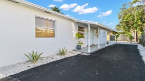 A two-story house with a covered porch, a driveway, and a small garden area. - "Sunflower Cottage Apt" 2/1 (West Palm Beach)