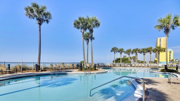 A swimming pool with a 3 FT depth marker, surrounded by palm trees and lounge chairs, with a clear blue sky in the background.