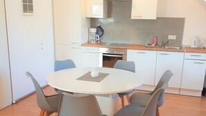 A modern kitchen with white cabinets, a round dining table with four chairs, and a visible oven. - Vacation home Südwind - Maisonette apartment no. 2 (Rhauderfehn)
