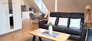 A modern living room with a black leather sofa, a wooden coffee table, and a dining area with a table and chairs.