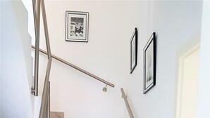 A staircase with a metal handrail, beige steps, and two framed pictures on the wall. - Vacation home Südwind - Maisonette apartment no. 2 (Rhauderfehn)