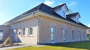 A two-story brick building with a flat roof, multiple windows, and a small garden area in front. - Vacation home Südwind - Maisonette apartment no. 2 (Rhauderfehn)
