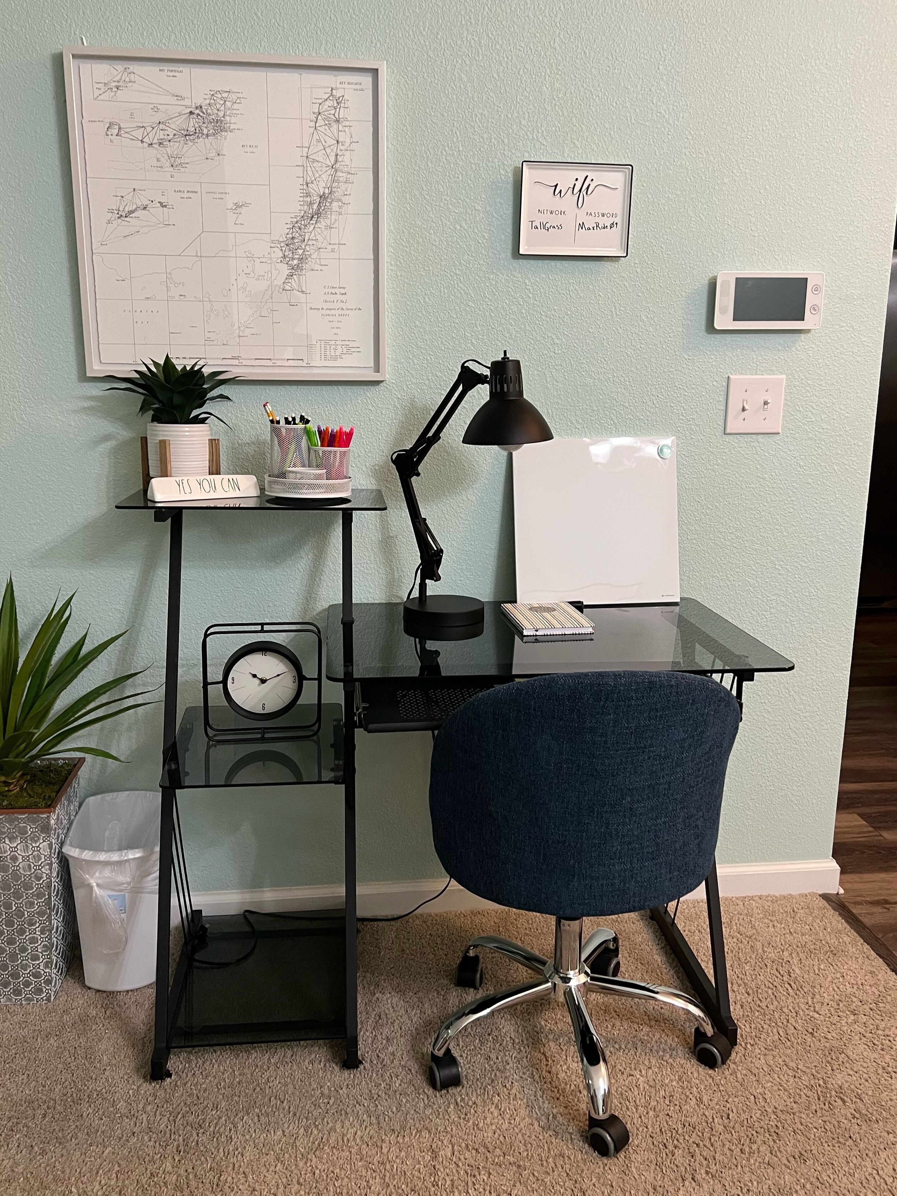 A home office setup with a desk, chair, clock, desk lamp, potted plants, and motivational signs.